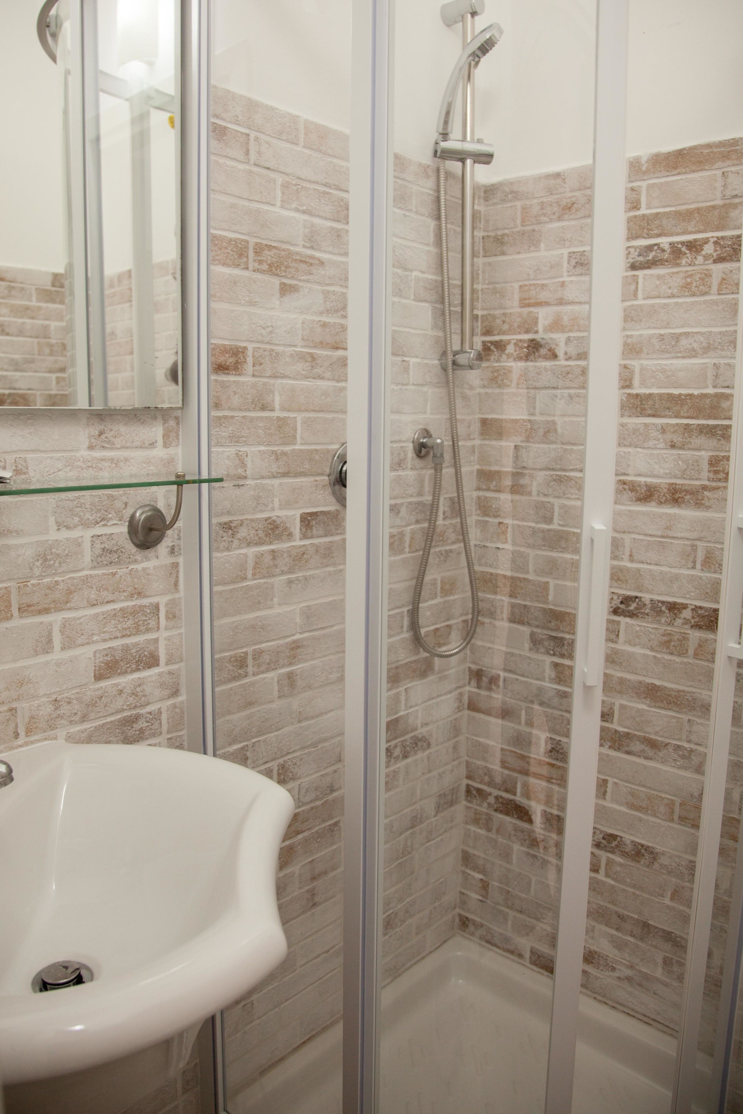 Une salle de bain avec une douche à parois de verre, un lavabo blanc et un mur décoré d’un motif en briques.