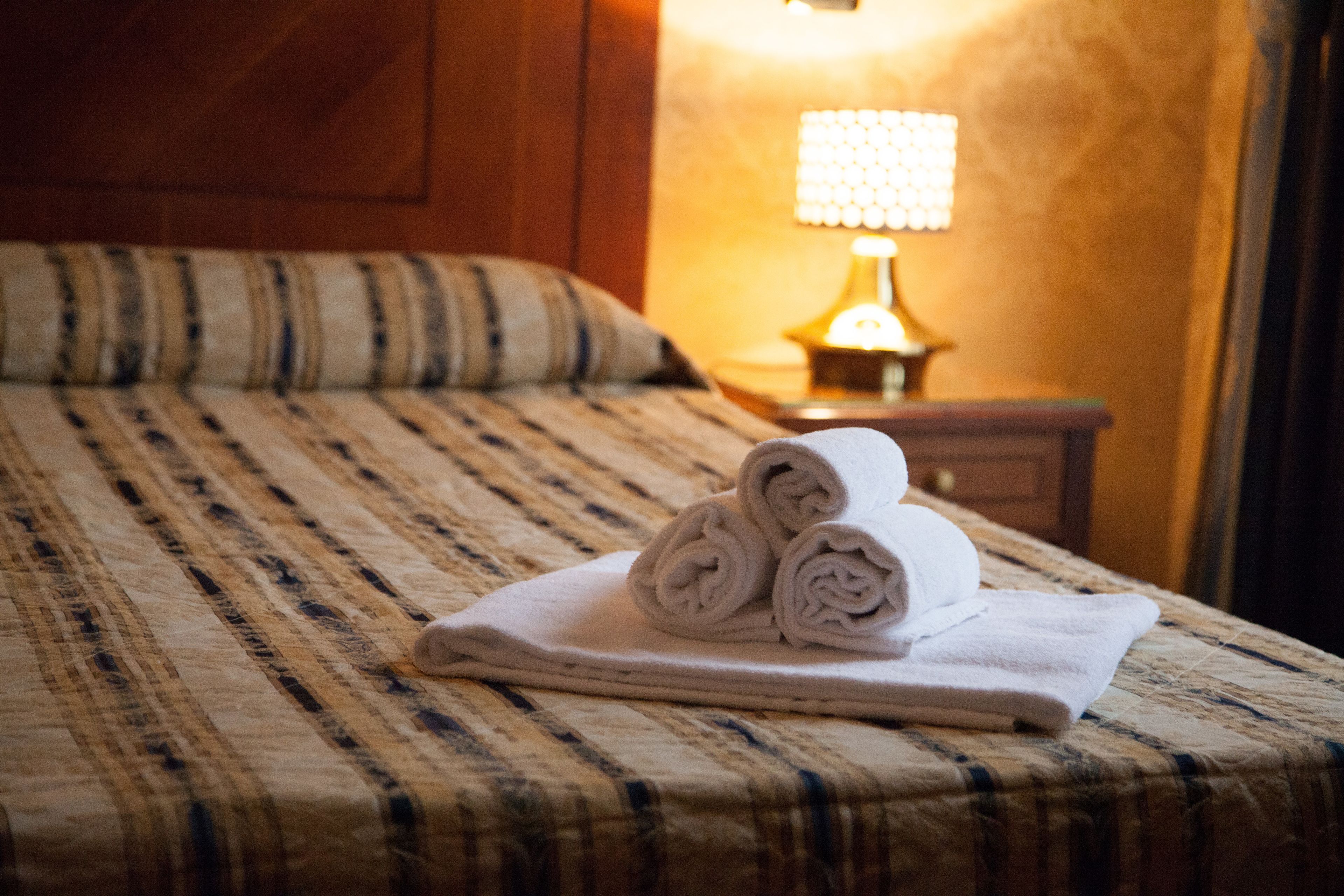 Un lit bien fait, avec une couvre-lit à rayures et des serviettes enroulées posées sur un oreiller blanc.