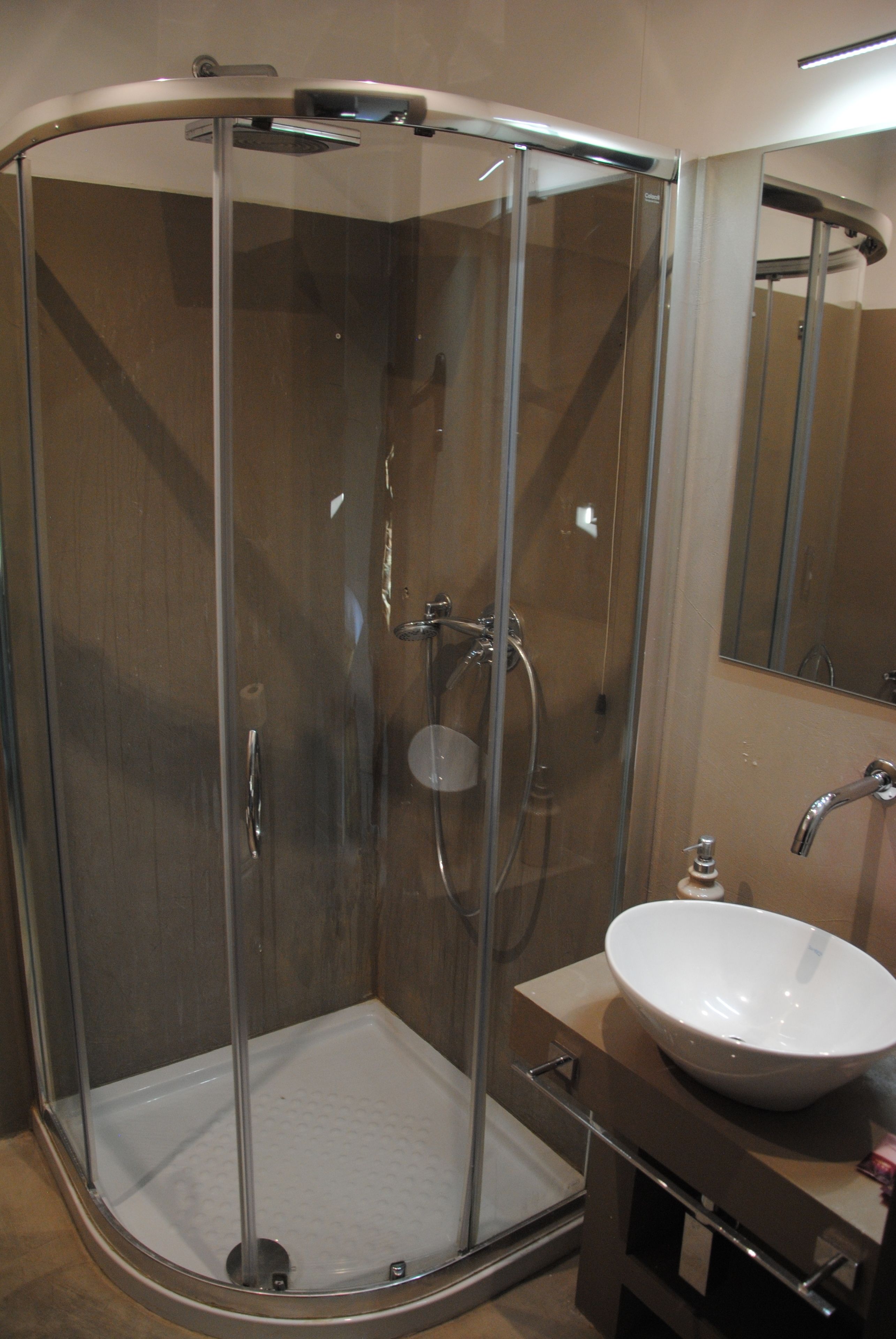 A modern shower enclosure with a glass door, a handheld showerhead, and a wall-mounted faucet.