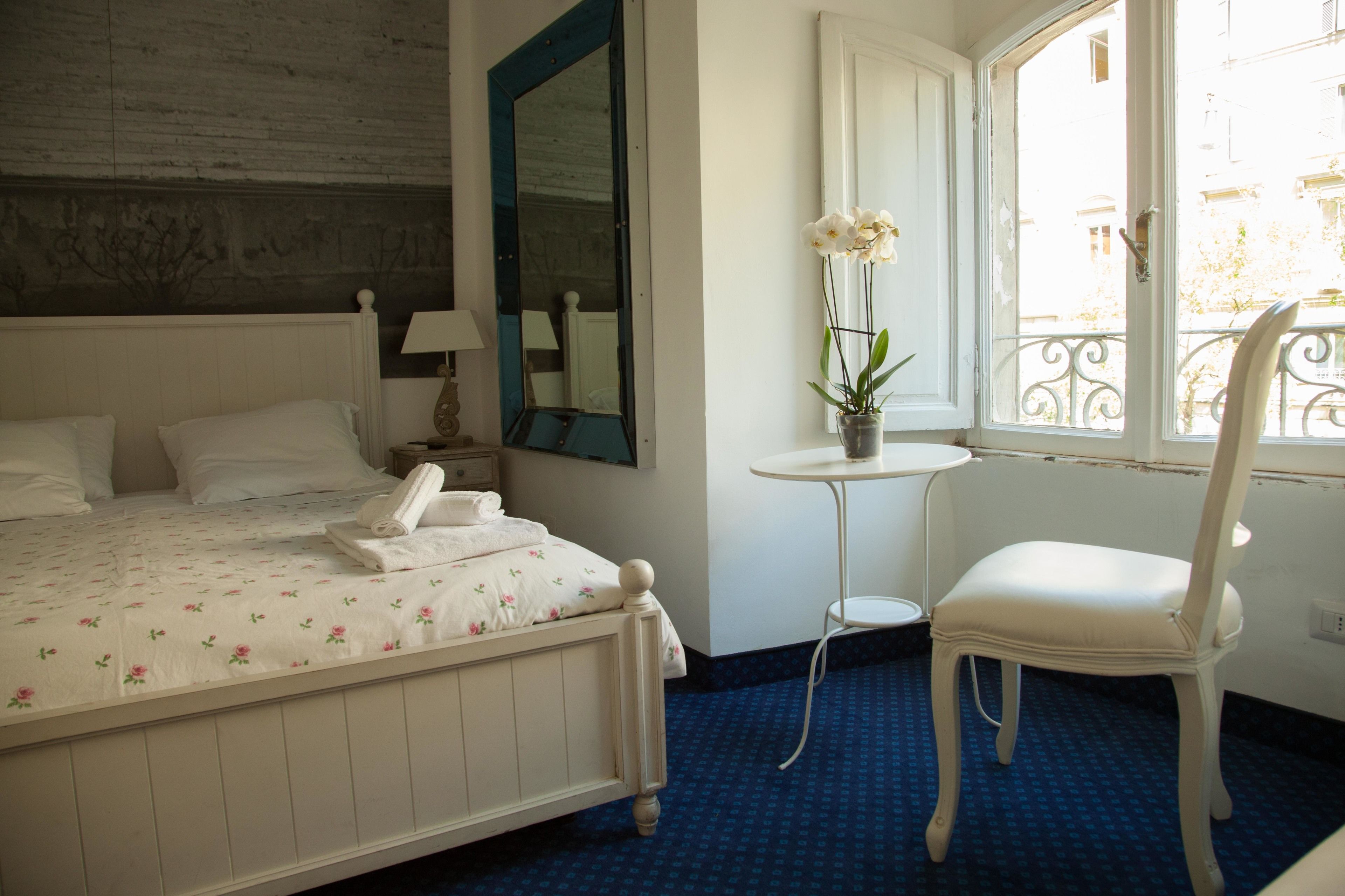 A hotel room with a bed, a chair, a small table, a mirror, and a window with a view of the outside.
