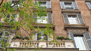 A multi-story building with a classic architectural style, featuring a prominent arched entrance, multiple windows with shutters, and decorative balconies with potted plants. - White Vatican (Rome)