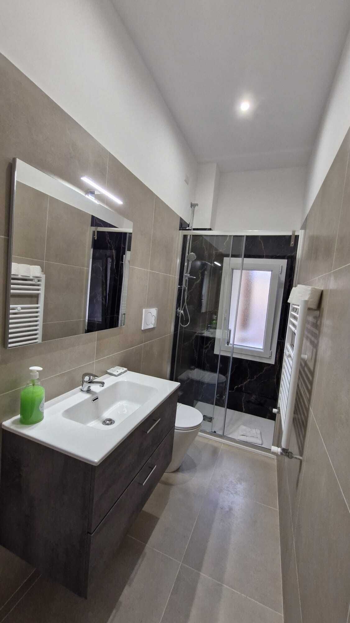 A modern bathroom with a large mirror, a vanity with a sink, a shower enclosure, and a toilet.