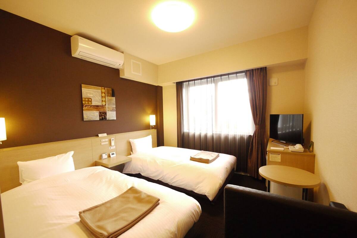 Habitación de hotel con dos camas, un escritorio, un televisor y una ventana con cortinas.