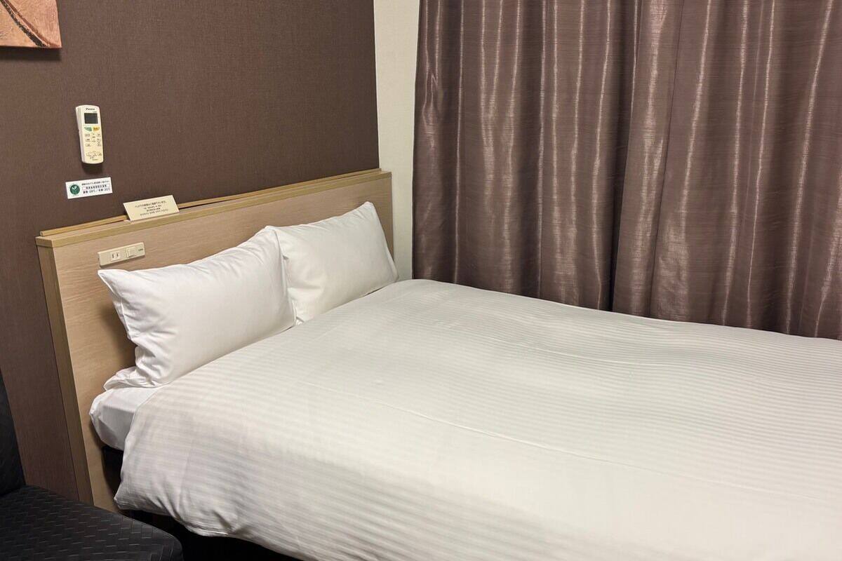 Una habitación de hotel con una cama, una mesita de noche, un panel de control y una cortina.