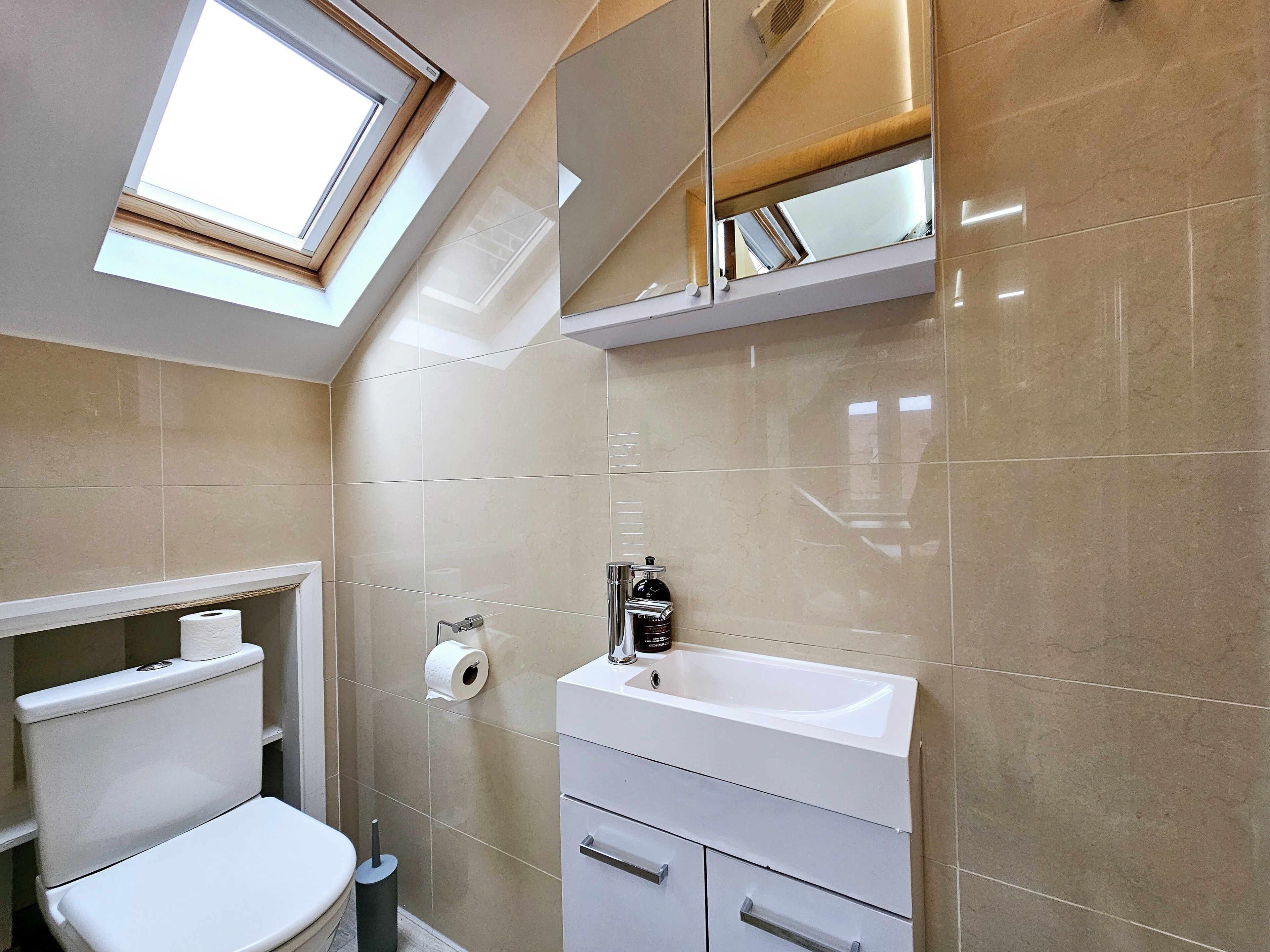 Een moderne badkamer met dakraam, toilet, wastafel met spiegel en een handdoekhouder.