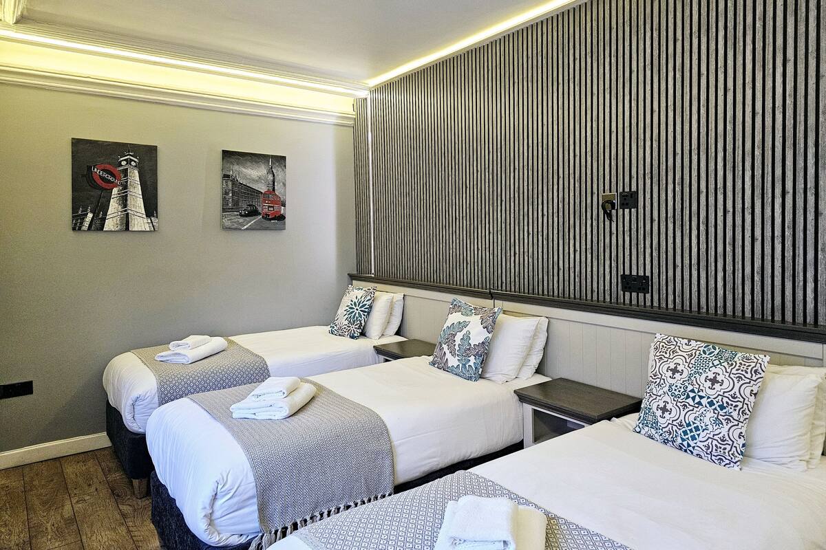 Ein Hotelzimmer mit zwei Betten, einer großen, gestreiften Wand und Kunstwerken, die einen roten Doppeldeckerbus zeigen.