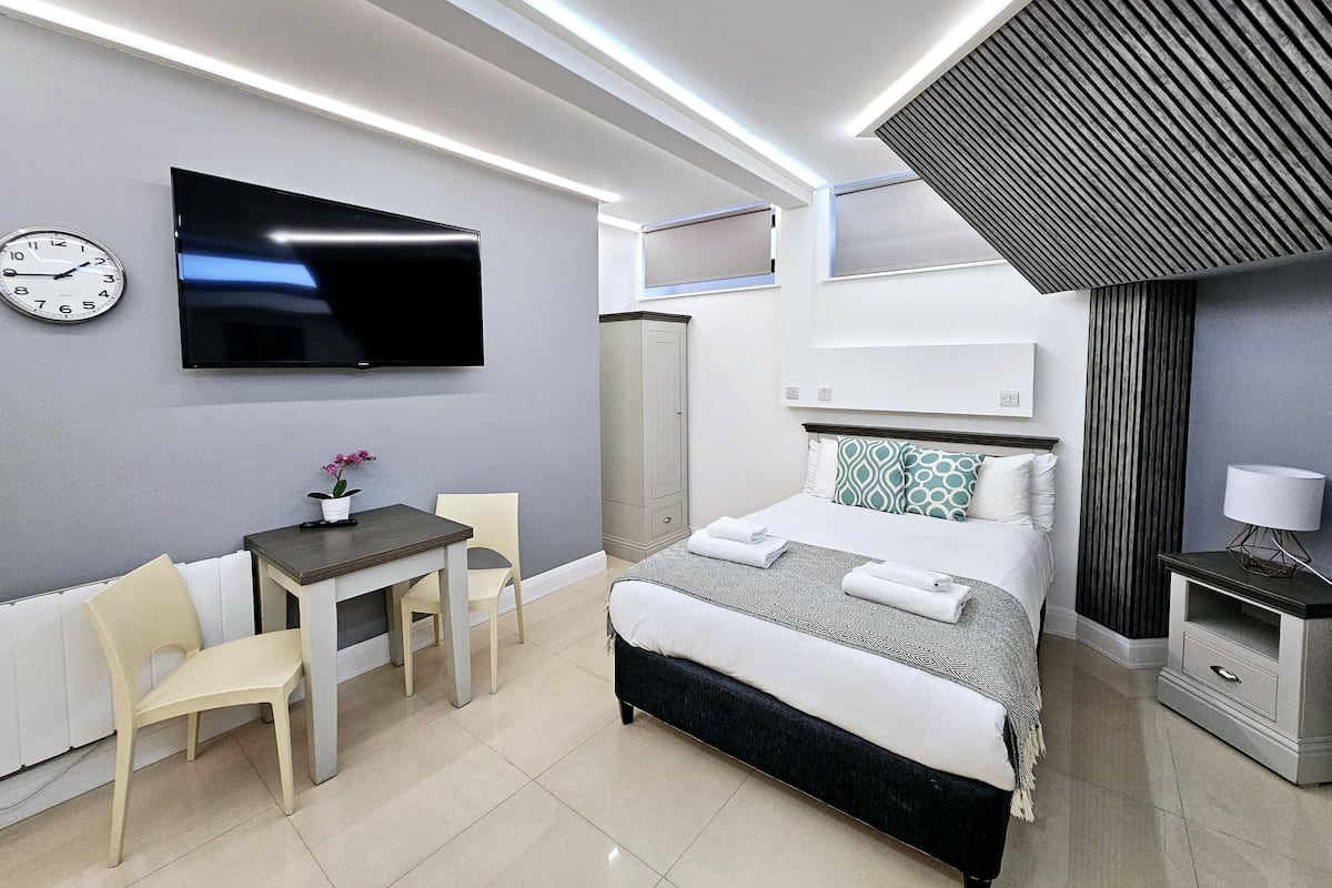 Ein modernes Hotelzimmer mit Bett, Schreibtisch, Stuhl, Fernseher und einer Wanduhr.