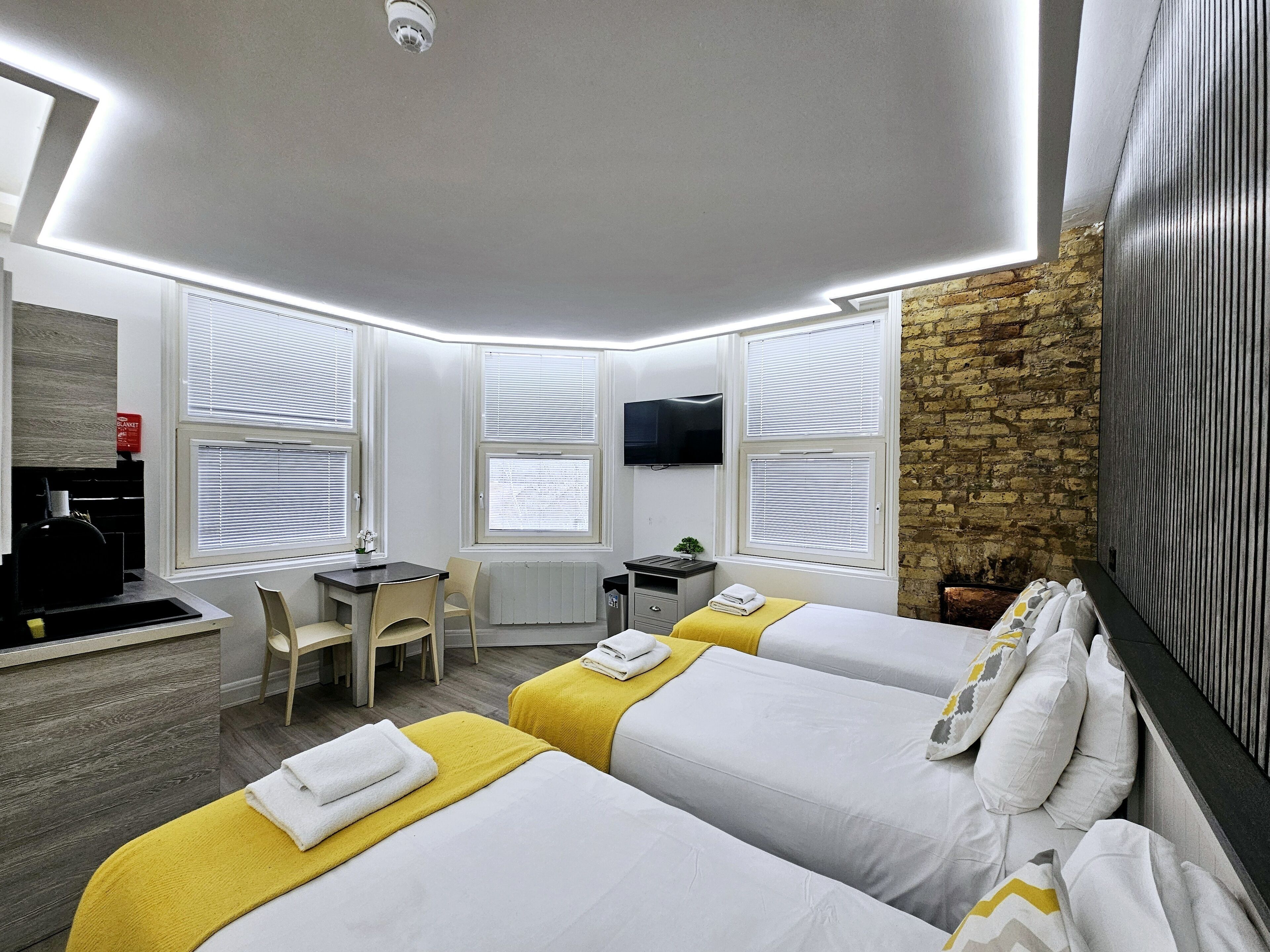 A hotel room with two beds, a desk, a chair, a TV, and a stone wall.