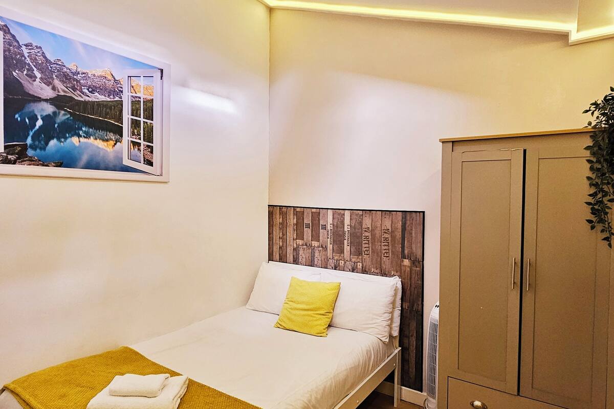 Ein Schlafzimmer mit einem Bett, einem Holz-Kopfstück, einem Kleiderschrank, einem Fenster mit Blick auf Berge und einem Nachttisch mit einer Lampe.