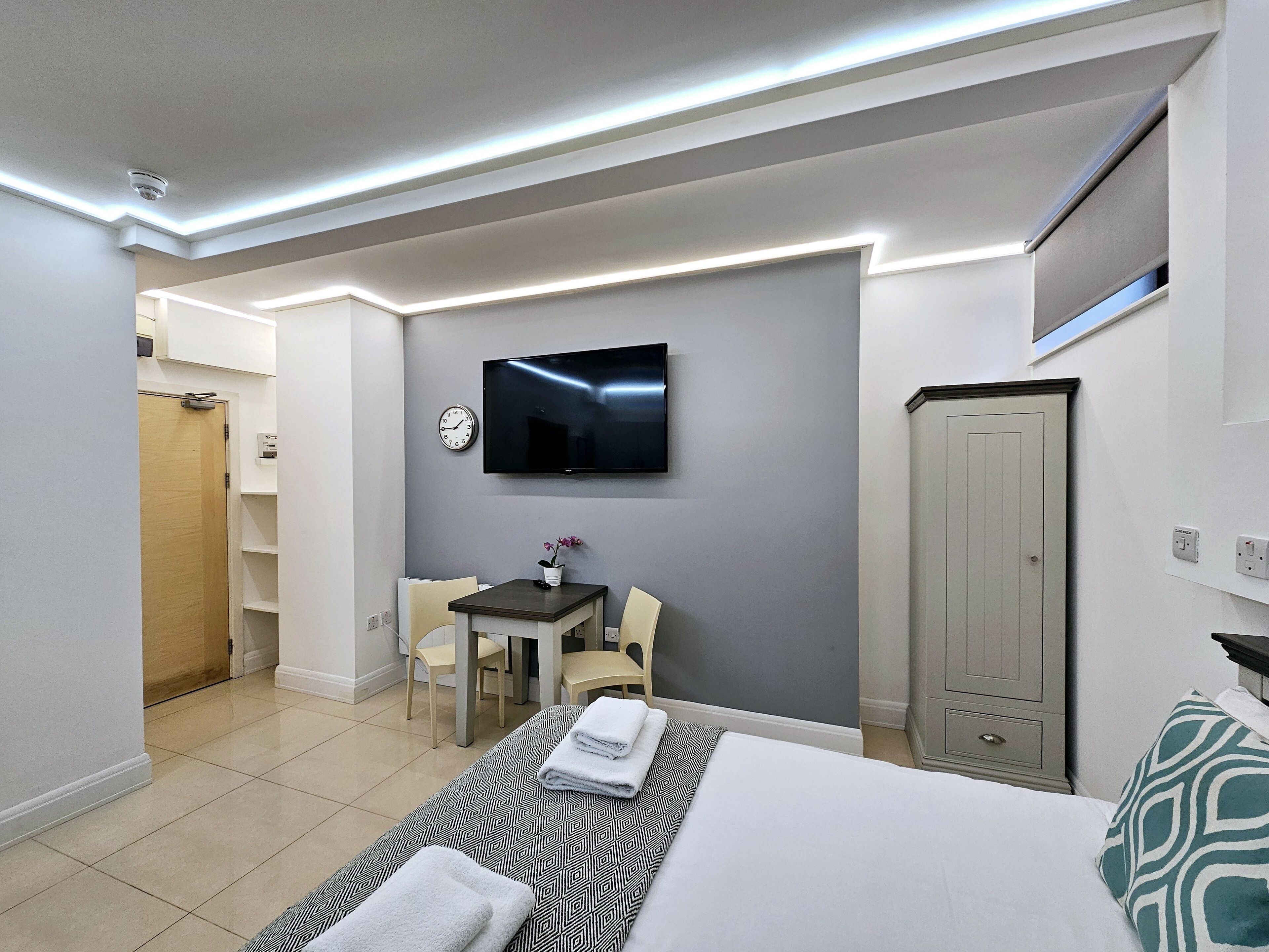 A modern hotel room with a bed, a desk, a chair, a TV, and a wardrobe.