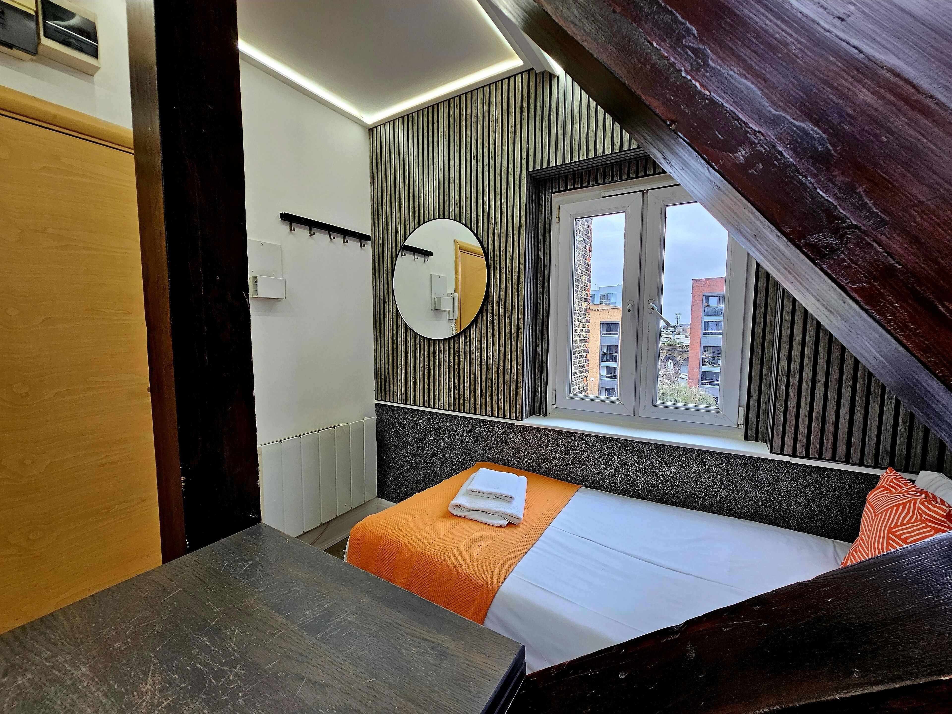 Un dormitorio con cama, un espejo redondo, una ventana y un radiador.