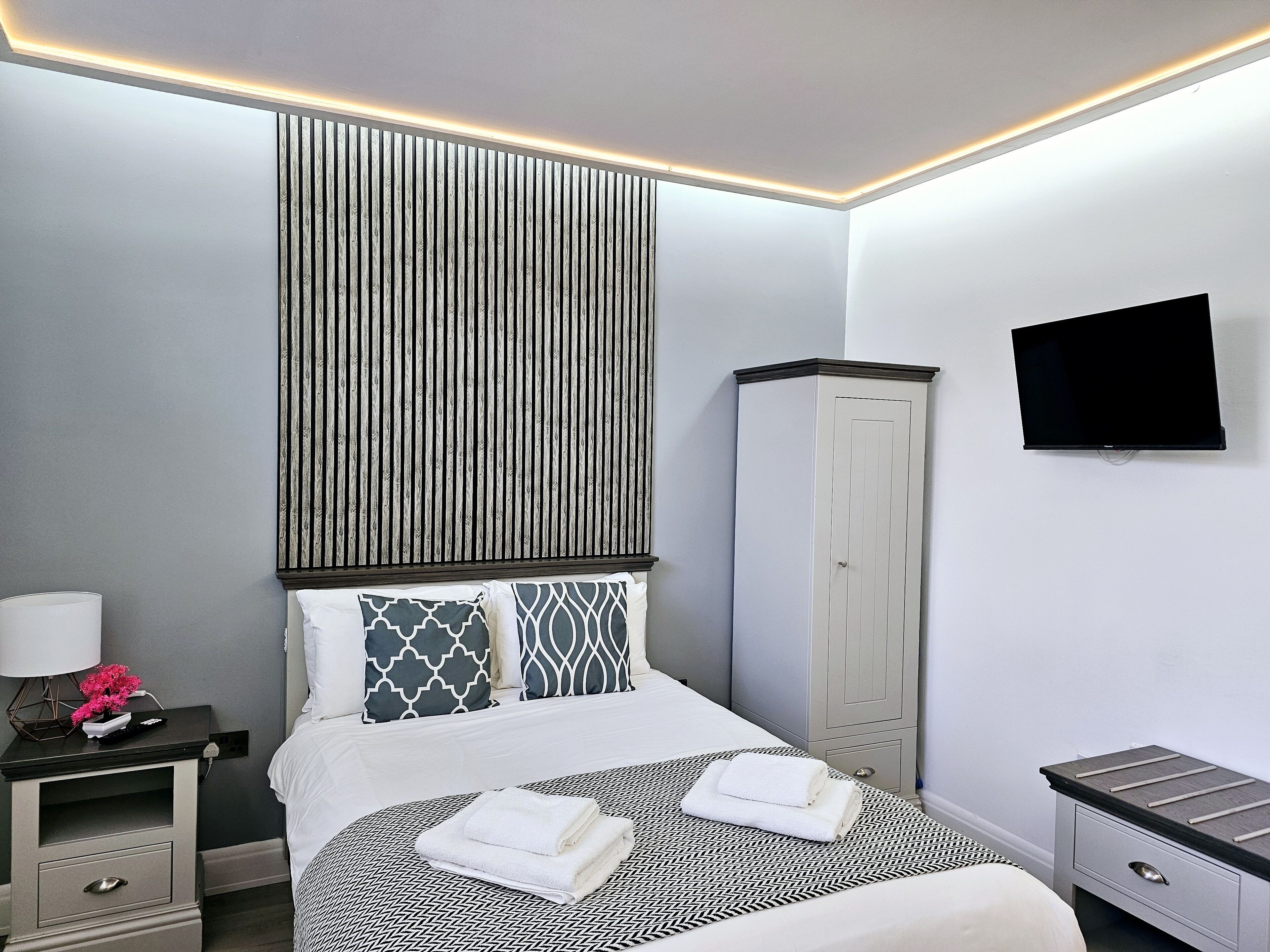 A modern hotel room with a bed, bedside tables, a wardrobe, and a TV mounted on the wall.