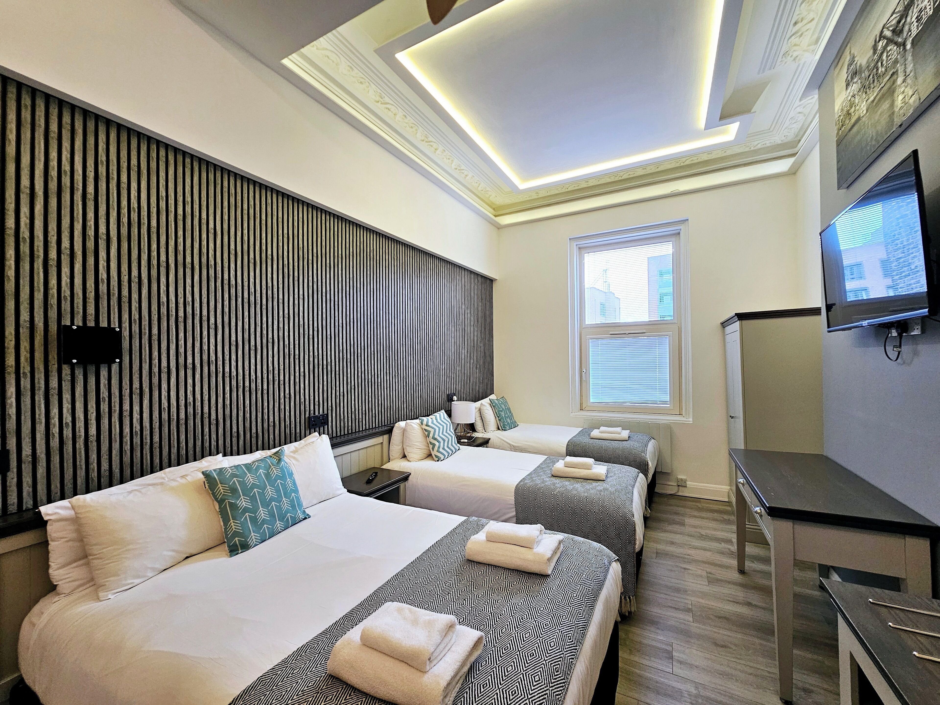 Une chambre d’hôtel avec deux lits, une télévision et une fenêtre avec des stores.
