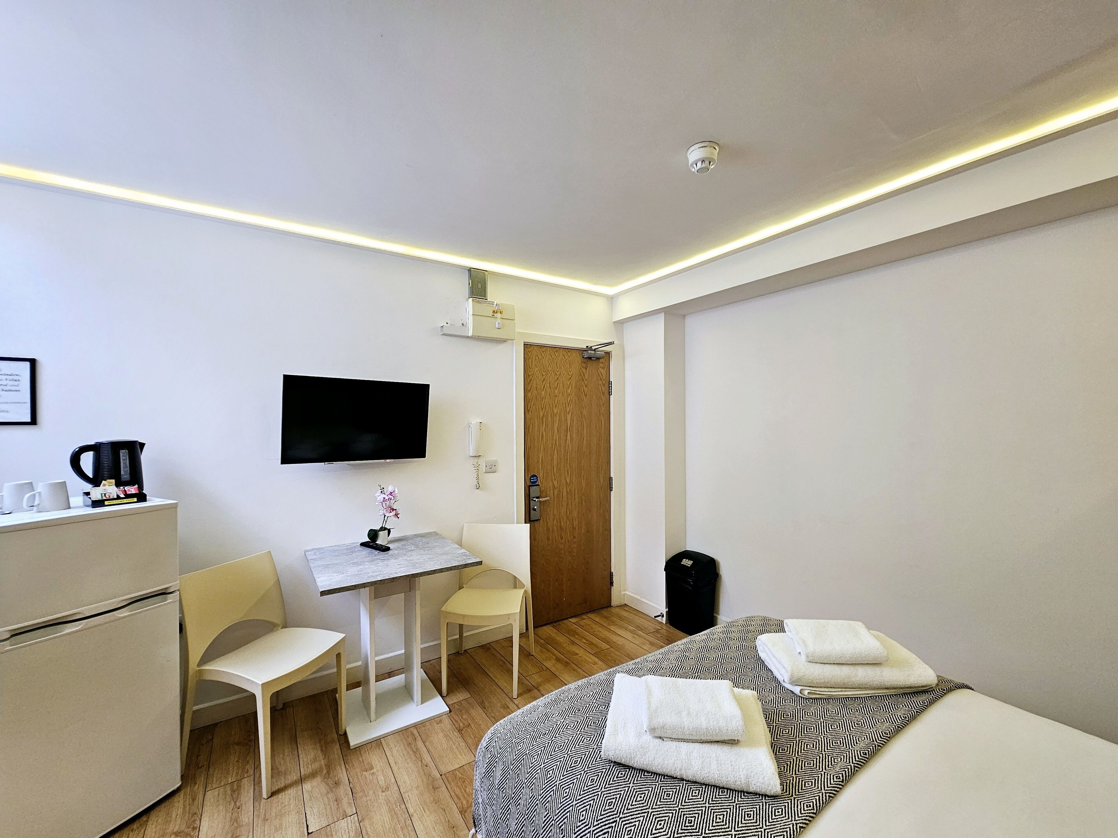 Habitación de hotel pequeña con cama, escritorio con silla, televisor y una mesita con un florero.