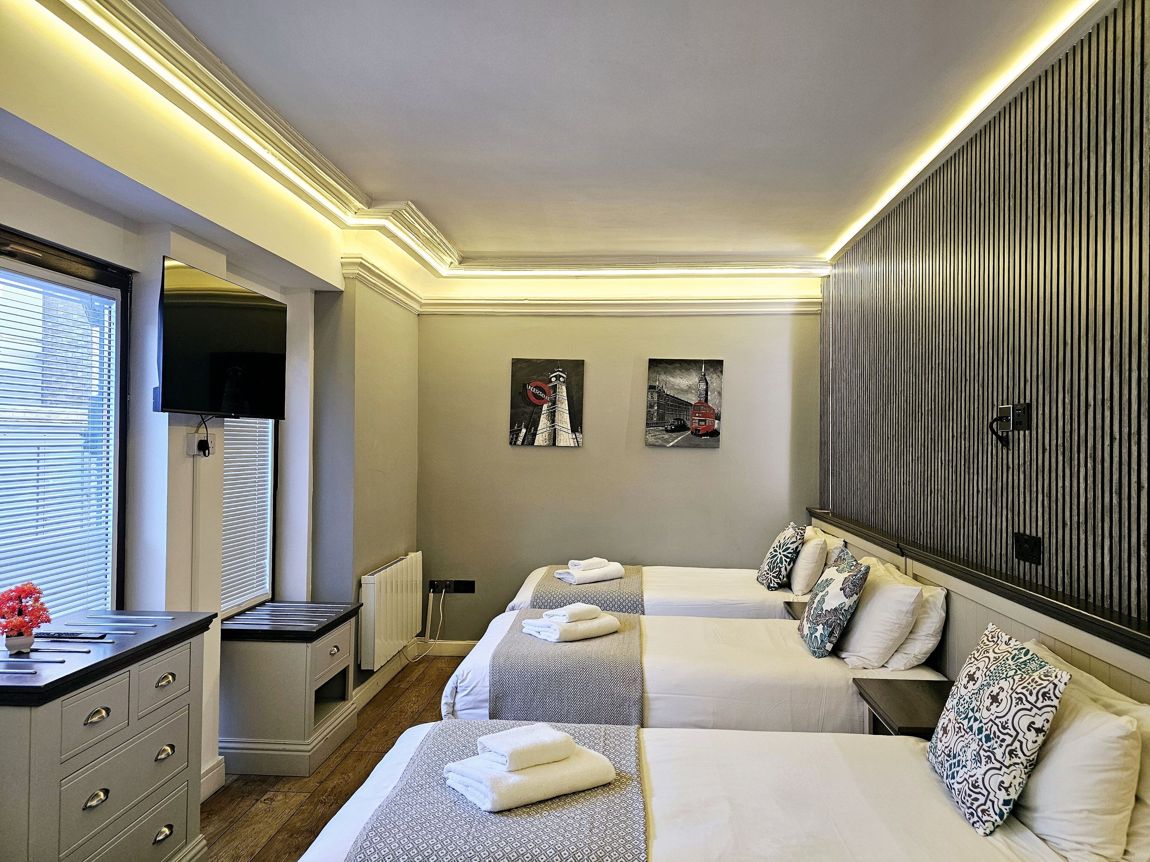 A hotel room with two beds, a dresser, a window with blinds, and artwork on the walls.