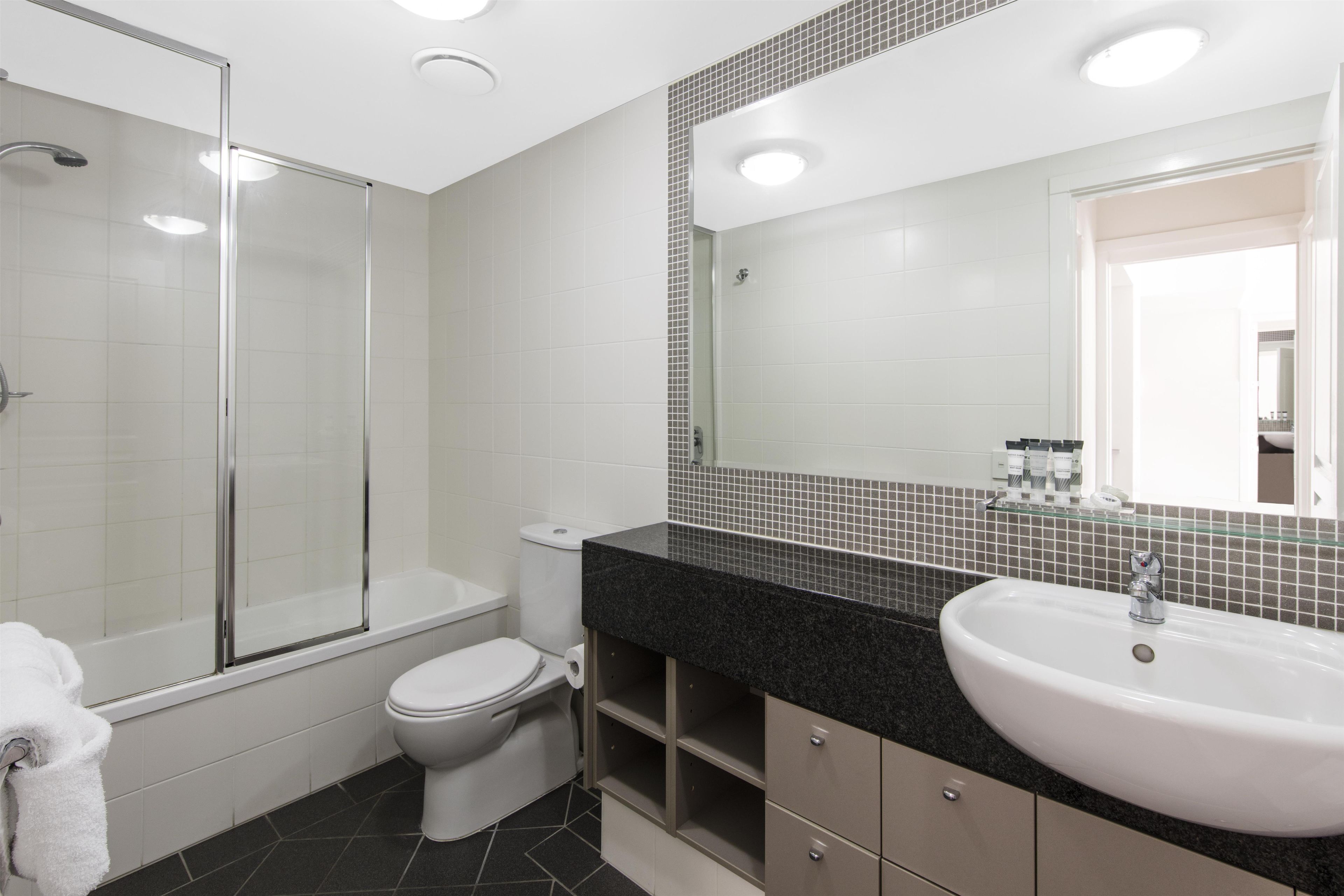 A modern bathroom with a glass shower enclosure, a white toilet, and a sink with a black countertop.