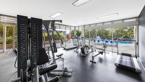 A gym with various exercise equipment, a pool visible through the windows, and a view of the outside.