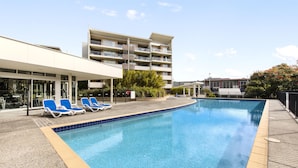 A swimming pool with lounge chairs and a building with multiple balconies in the background.
