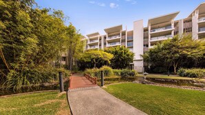 A pathway leading to a modern apartment building with multiple balconies and a well-maintained garden area.