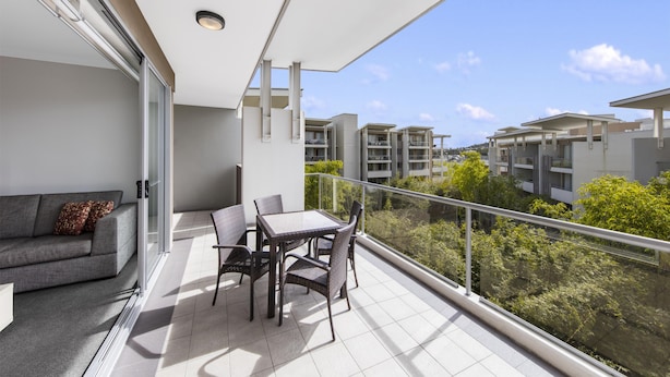 A balcony with a sofa and table, overlooking a residential area with greenery and buildings.