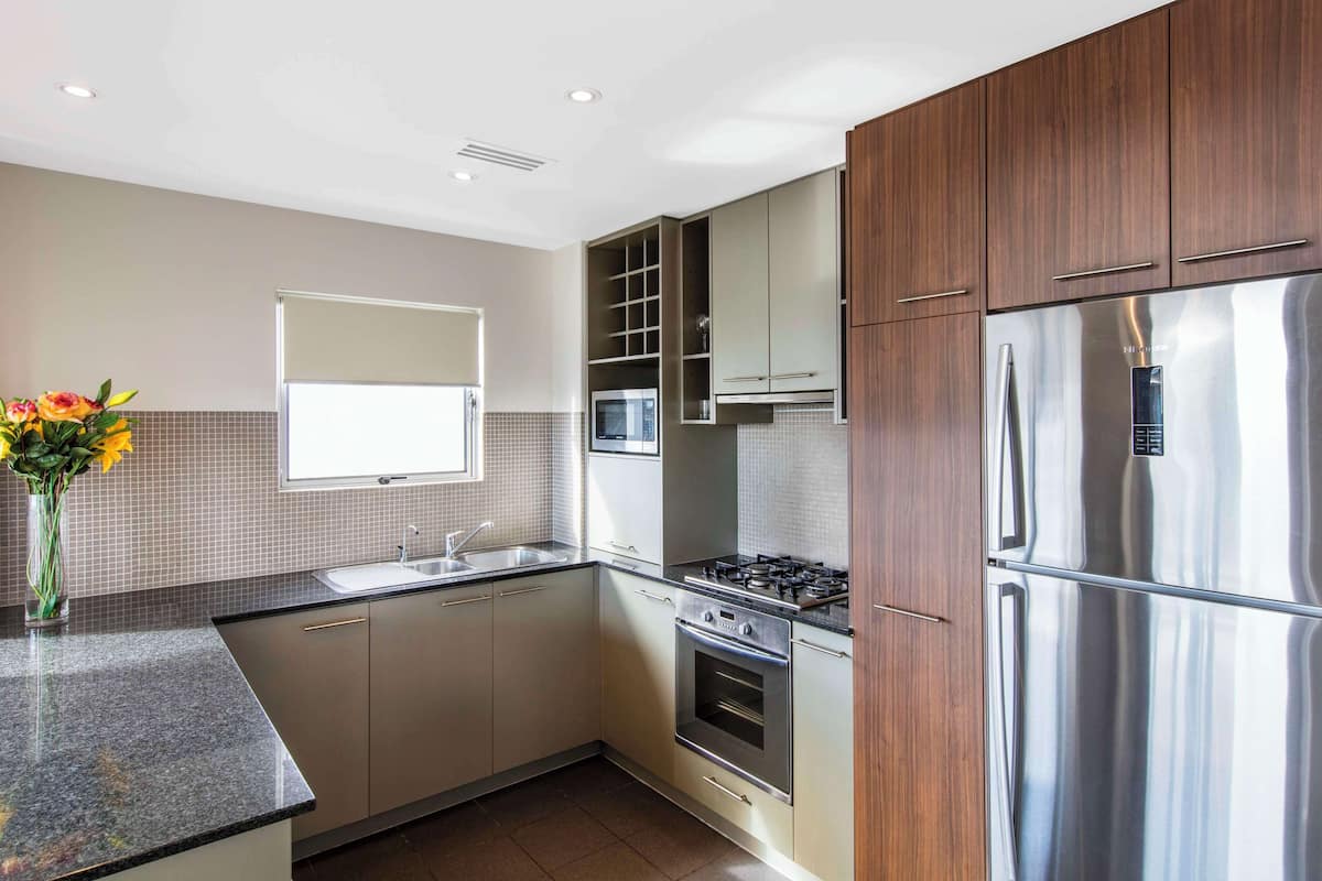 A modern kitchen with stainless steel appliances, wooden cabinets, and a granite countertop.