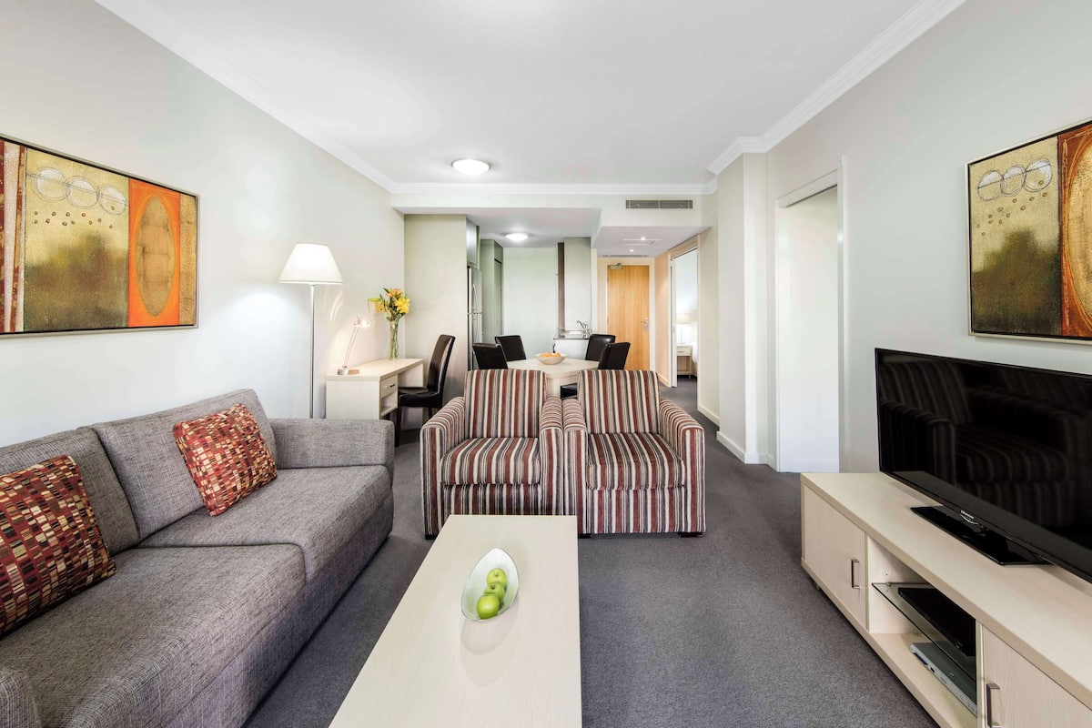 A modern living room with a sofa, a coffee table, a TV, and a dining area with chairs and a table.