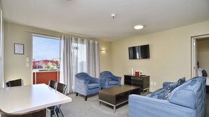 A modern living room with a dining table, two sofas, and a TV mounted on the wall. - The Riverstone (Rangiora)