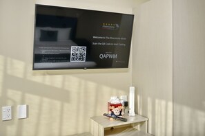 A television screen with instructions for starting a QR code scan, a remote control, and a small table with a plush toy and a tissue box. - The Riverstone (Rangiora)