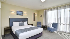 A hotel room with a large bed, a chair, a nightstand, and a window with curtains. - The Riverstone (Rangiora)