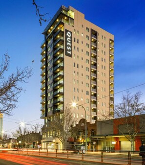 A tall, modern hotel with multiple floors and balconies, featuring a prominent 'QUEST' sign on the side.