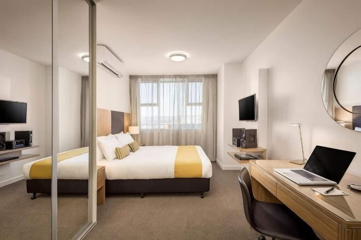 A hotel room with a bed, a desk with a laptop, a TV, and a mirror.