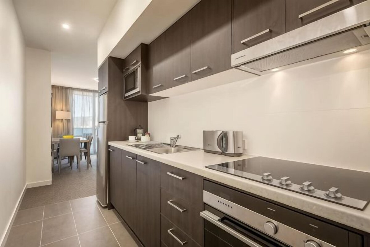A modern kitchen with dark cabinetry, stainless steel appliances, and a large countertop.