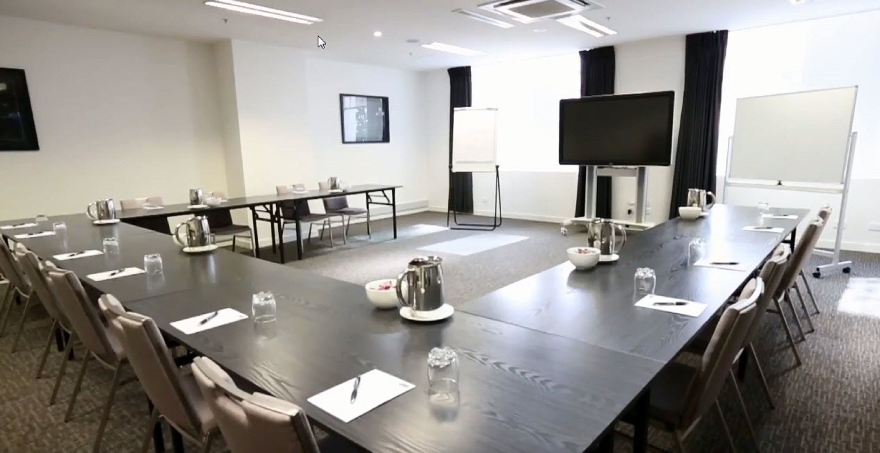 Een vergaderruimte met een lange tafel, stoelen, een televisie en een whiteboard.