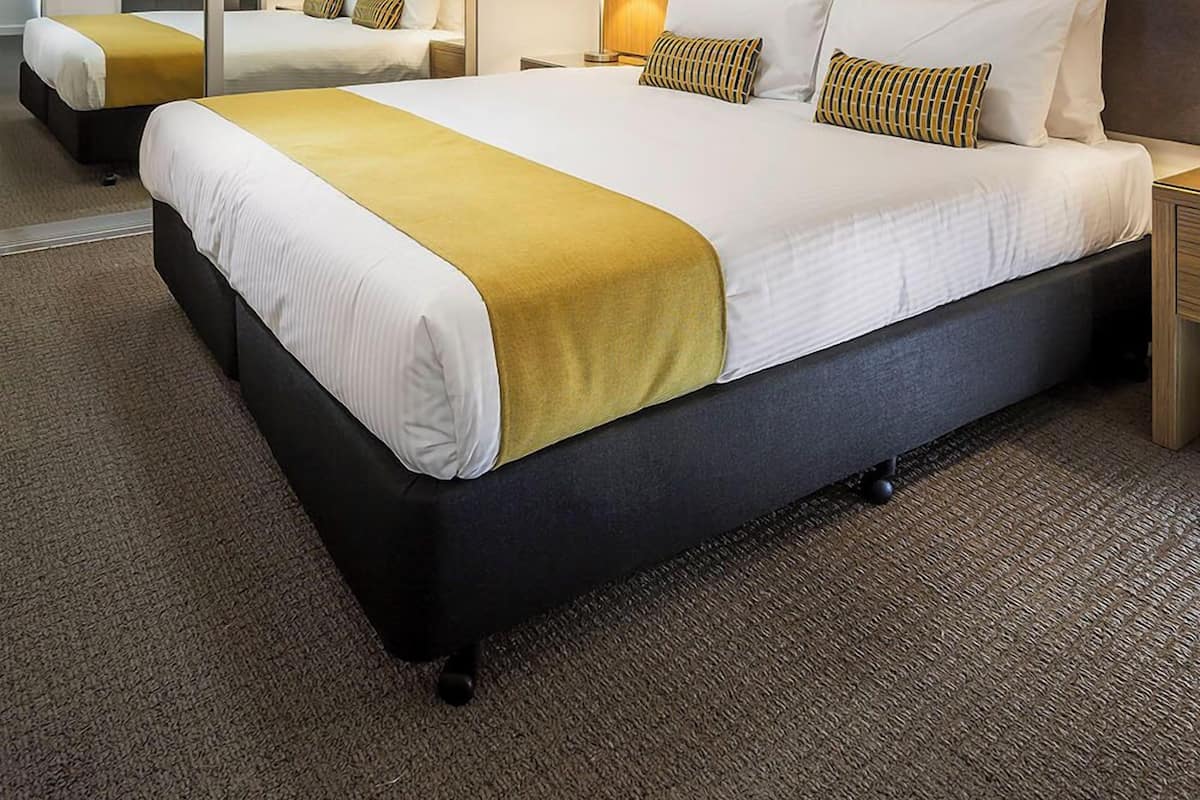 Quarto de hotel com uma cama grande, um espelho, uma mesa de cabeceira e uma luminária na parede.