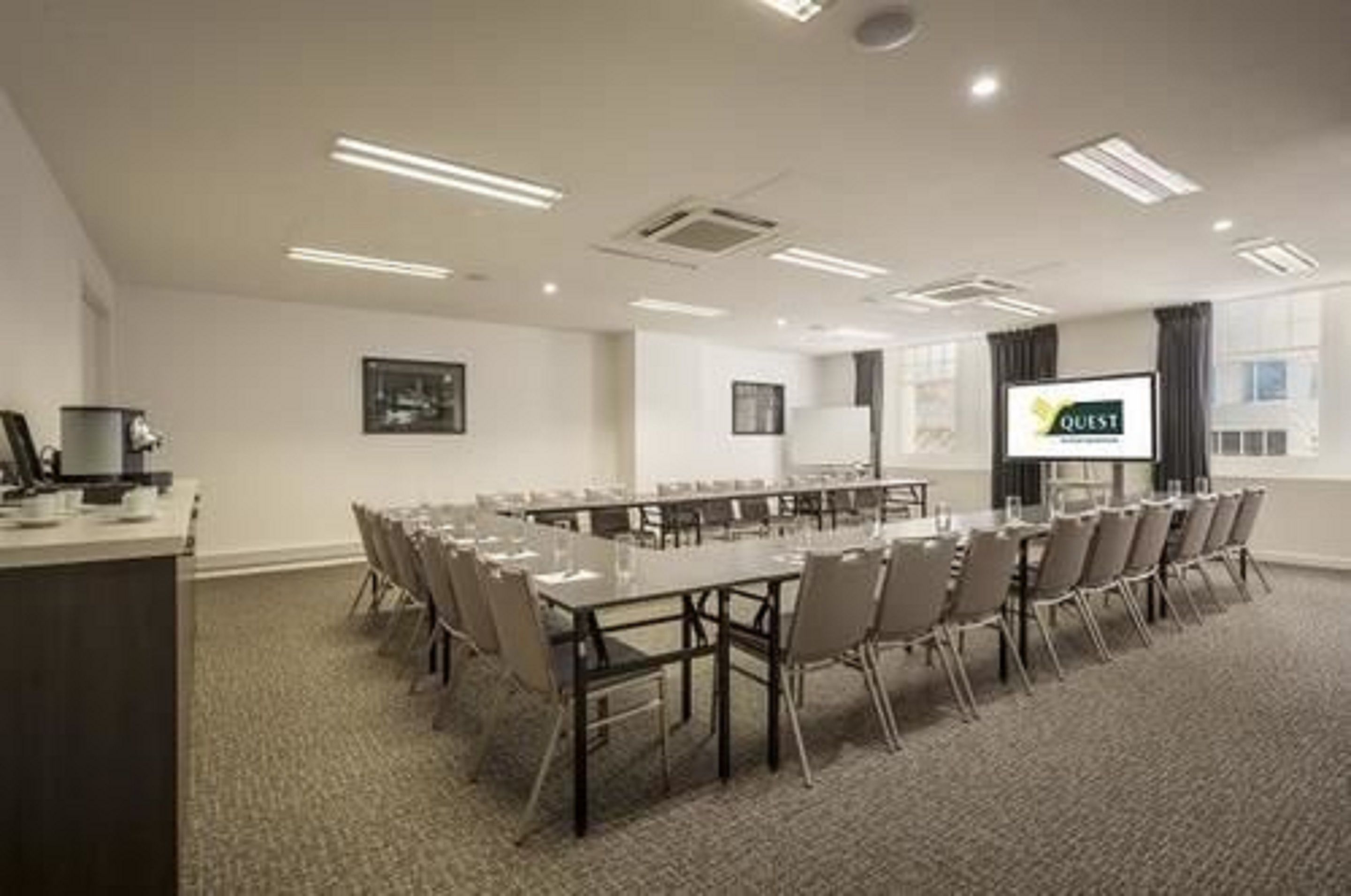 Ein Konferenzraum mit langem Tisch, Stühlen, einer Projektionsleinwand und einem Präsentationsbildschirm.