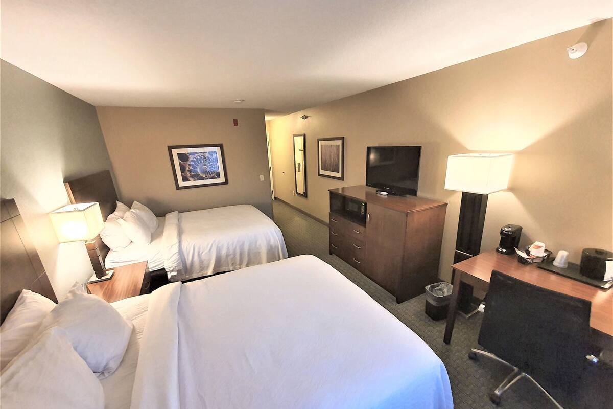 A hotel room with two beds, a desk, a chair, a TV, and a minibar.