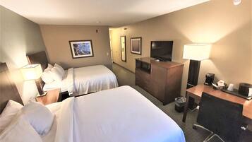 A hotel room with two beds, a desk, a chair, a TV, and a minibar.