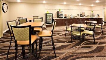Un comedor de hotel con varias mesas y sillas, un refrigerador y una estación de café.