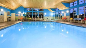 Una piscina interior con techo de madera y paredes azules, rodeada de sillas y ventanas.