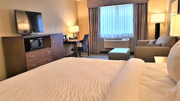 Habitación de hotel con una cama grande, un escritorio con silla, televisor, equipo de aire acondicionado y ventana con cortinas.