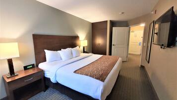 Quarto de hotel com uma cama grande, uma mesinha de cabeceira com abajur, um relógio digital e um guarda-roupa.