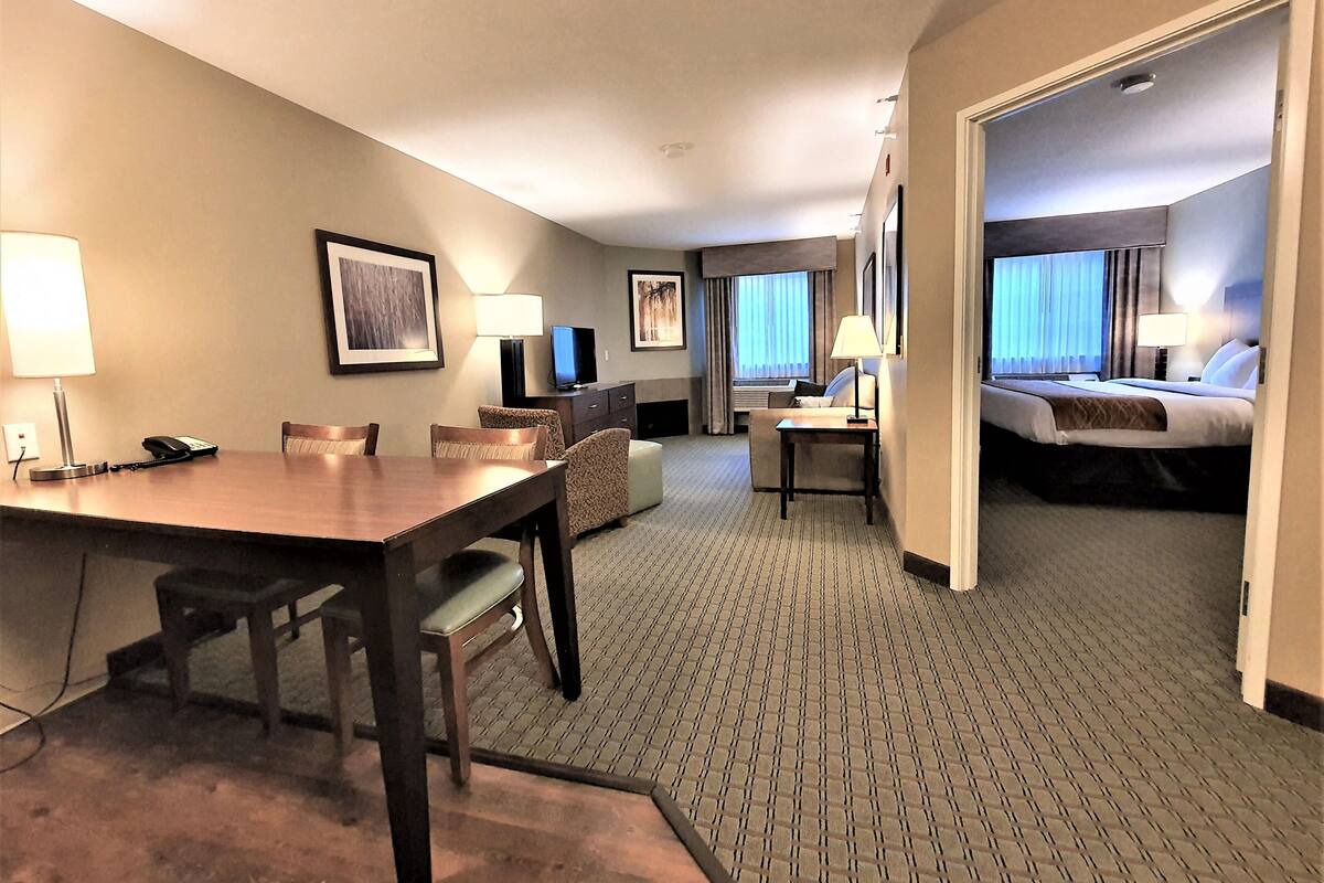 A hotel room with a bed, a desk, a chair, a TV, and a dining area with a table and chairs.