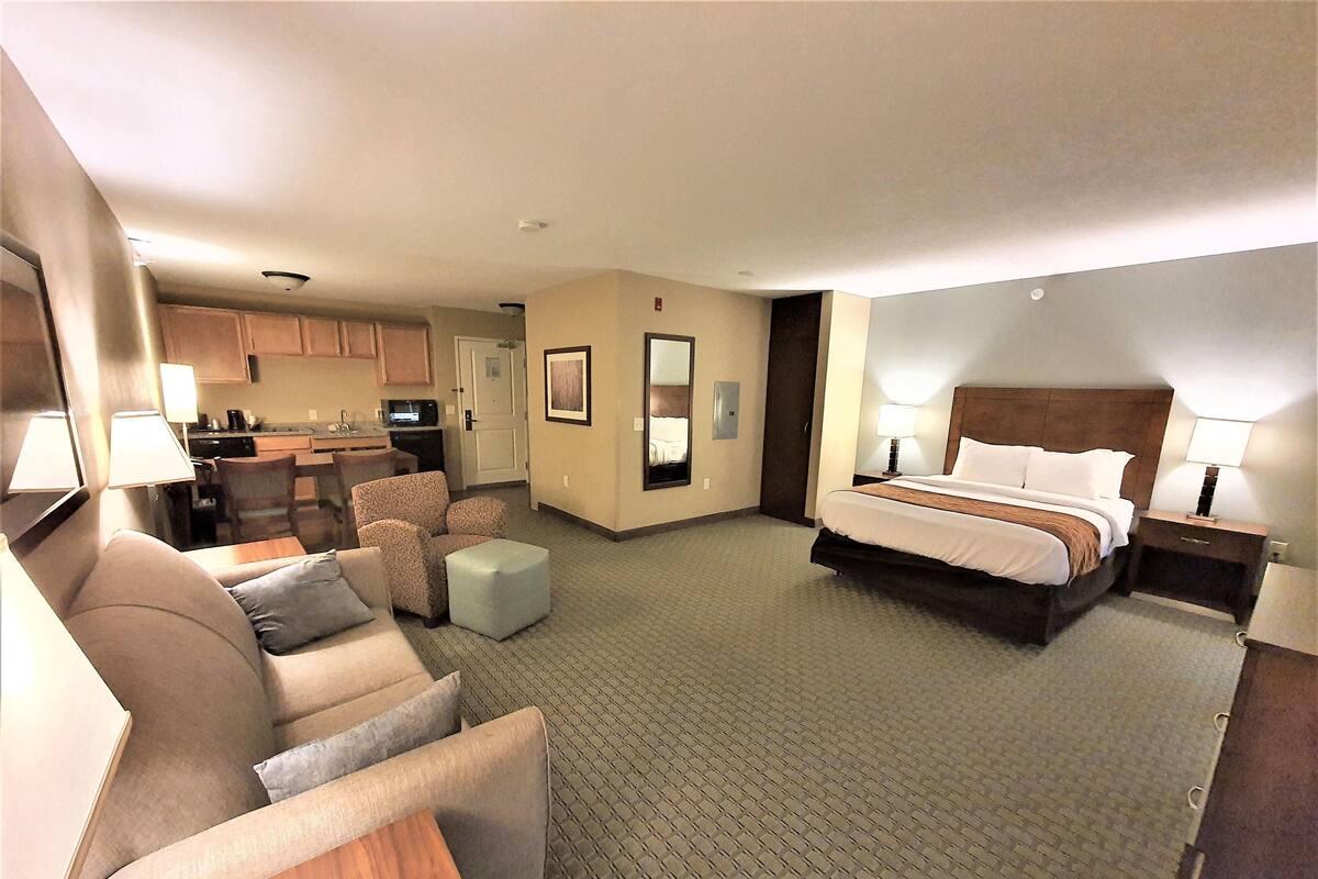 A hotel room with a bed, a sofa, a small table, a chair, a desk, and a kitchenette.