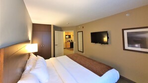 Habitación de hotel con una cama, televisor, un cuadro enmarcado y vistas de la cocina y el pasillo.