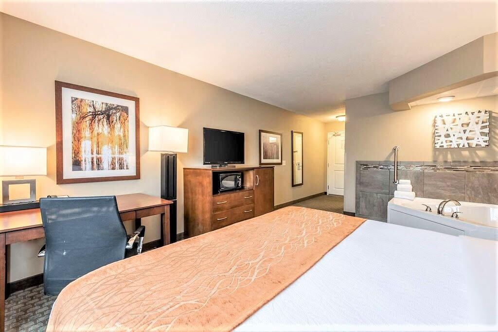A hotel room with a bed, desk, chair, TV, and a bathroom with a bathtub and shower.
