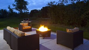 Un patio exterior con mobiliario de mimbre, una parrilla y un hogar para la chimenea.