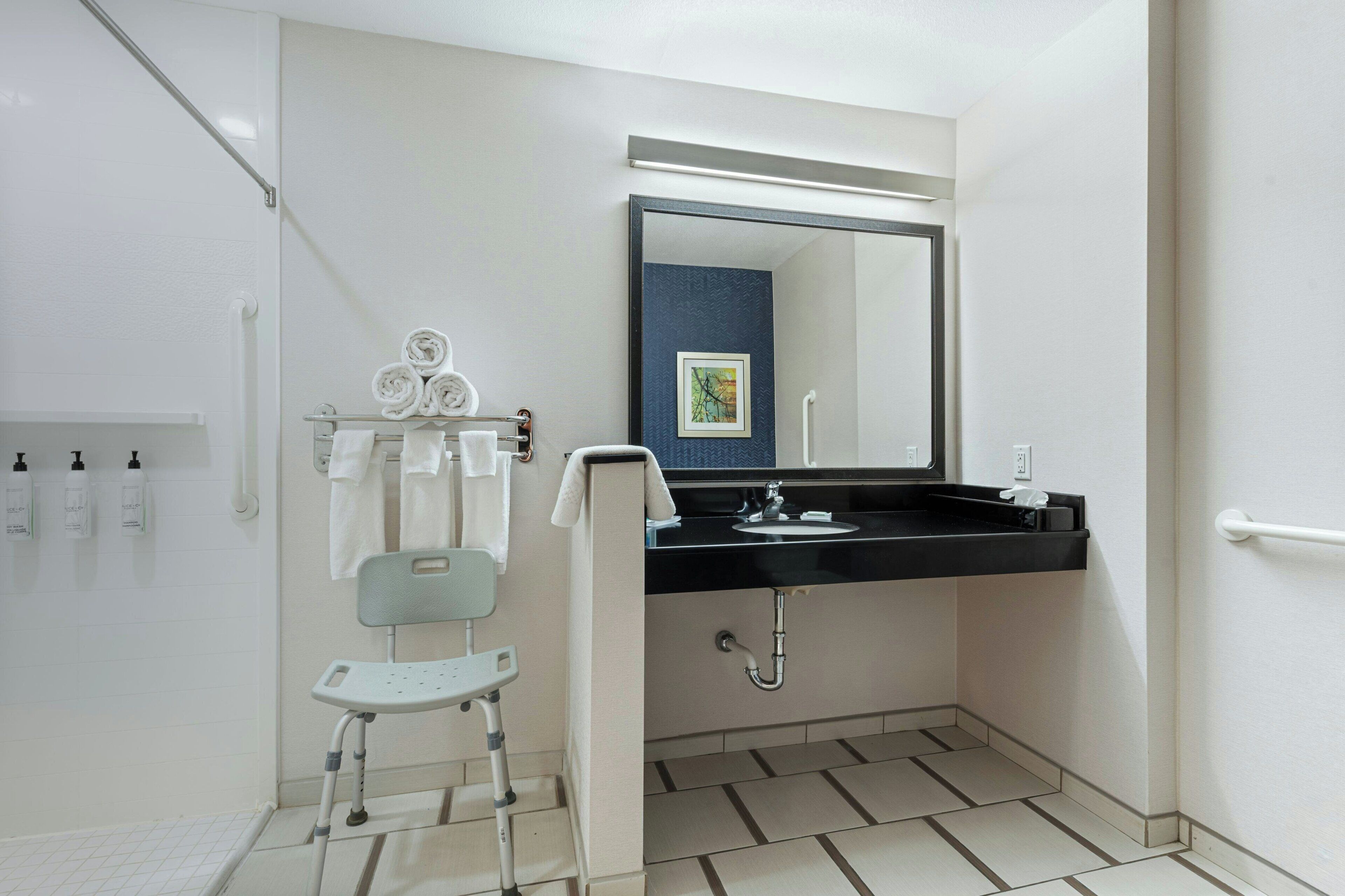 A modern bathroom with a wheelchair-accessible shower, a sink with a mirror, and a towel rack.