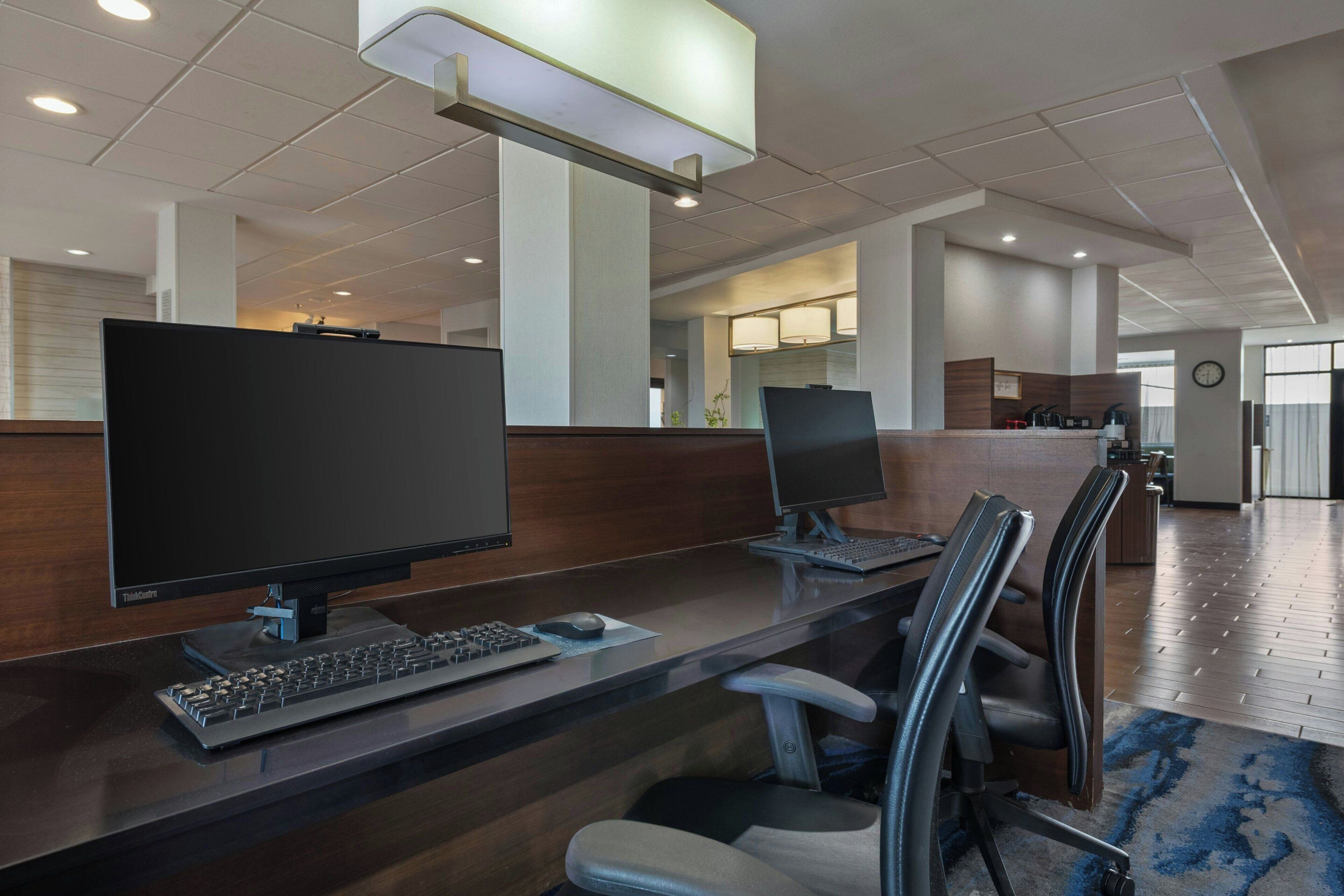 A modern hotel lobby with two computer workstations, a reception desk, and a clock on the wall.