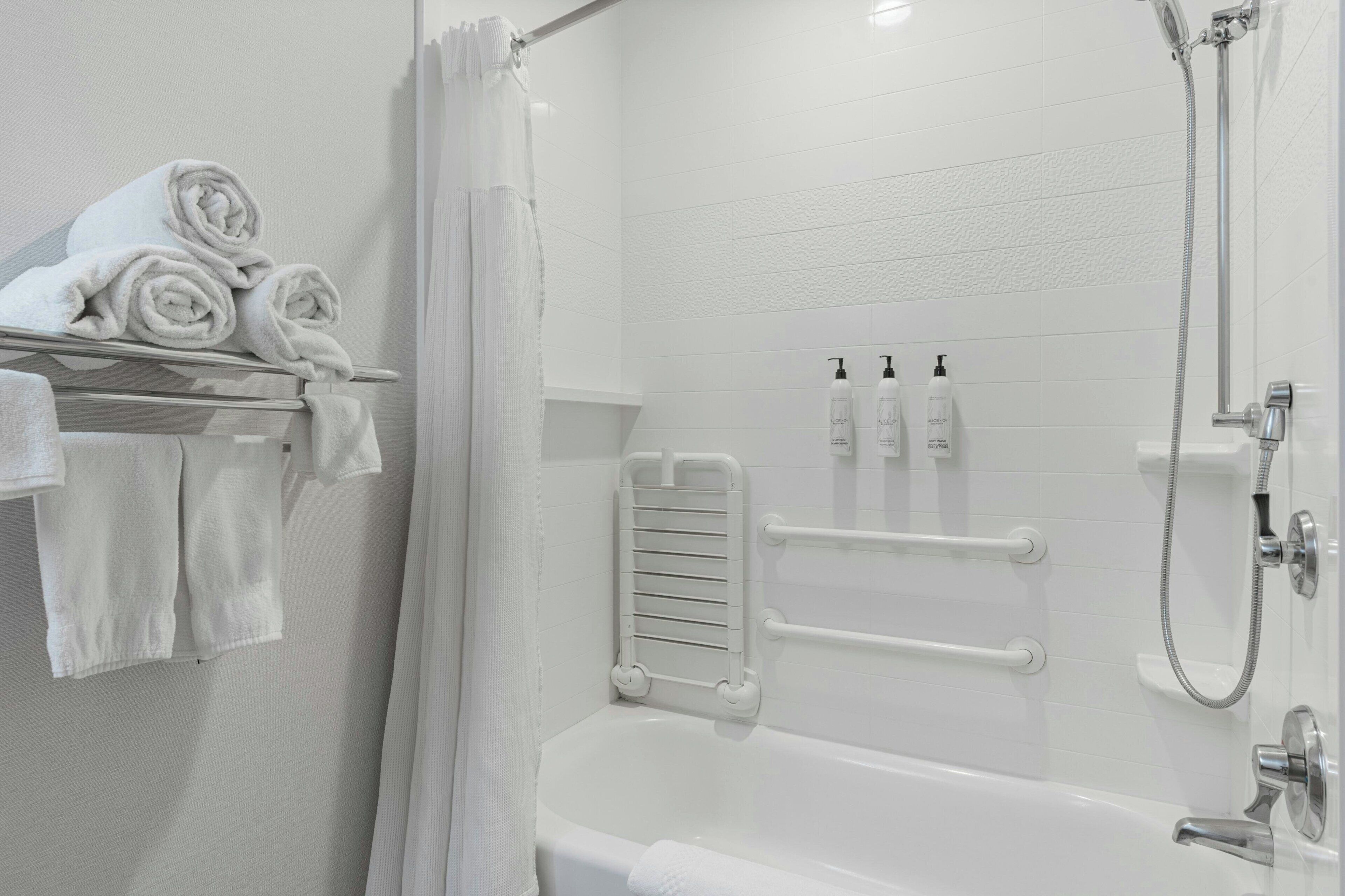 A modern bathroom with a white bathtub, a shower, and a towel rack with neatly rolled towels.