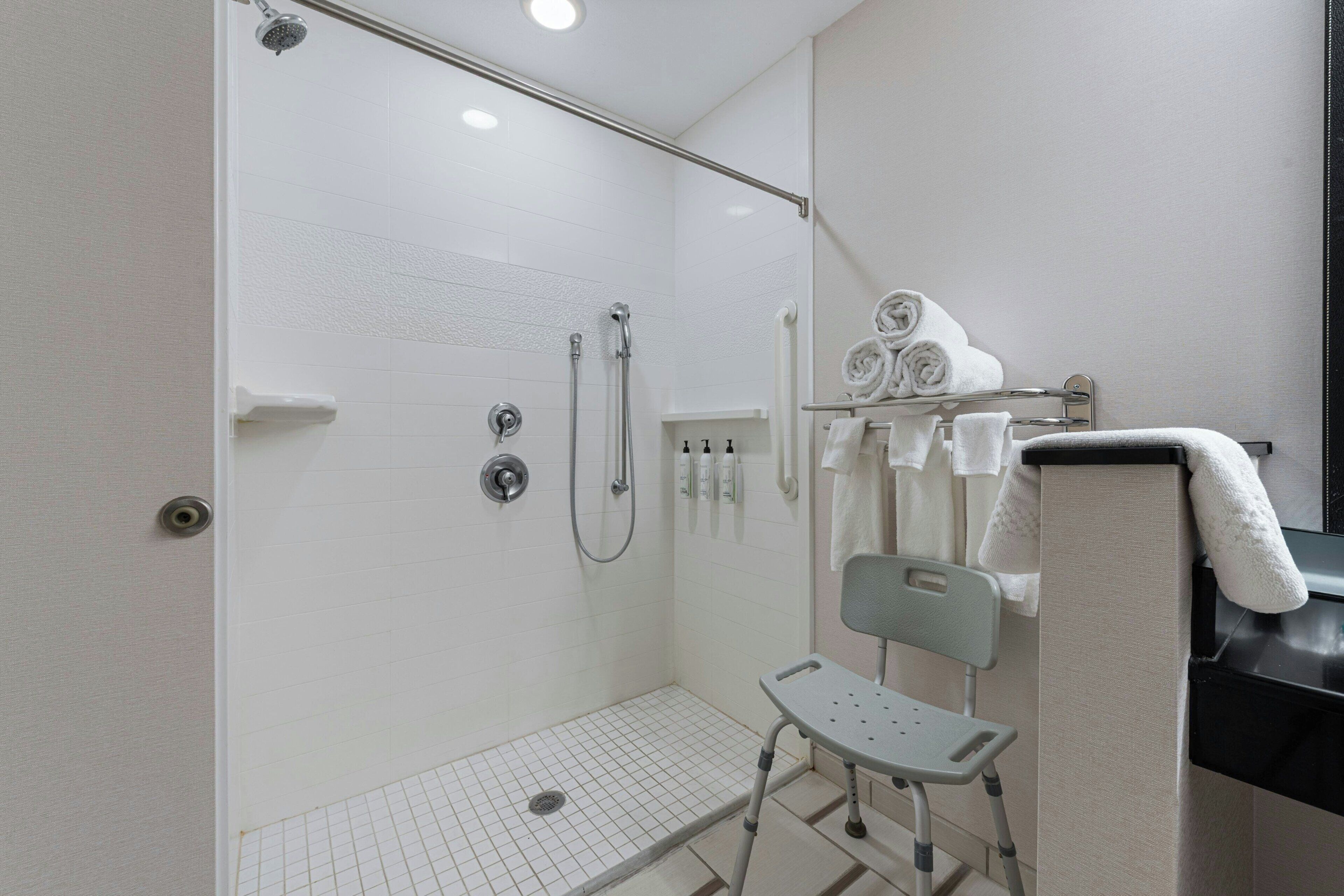 A shower with a glass door, a bench, and a towel rack with towels.